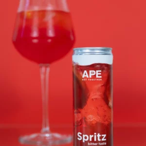 Image of a can of spritz bitter in the foreground and a glass of spritz bitter in the background. The background is light red, matching the colors of the can's graphics.